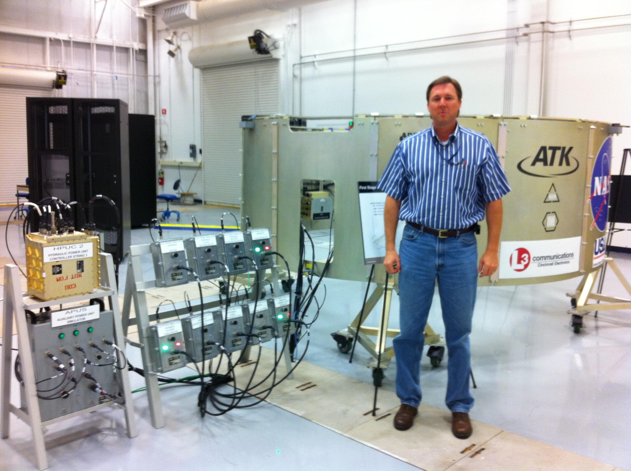 Ares I First Stage avionics hardware-in-the-loop test setup — HPUC hydraulic power controller and APUS auxiliary power simulator in front of the first-stage segment at the ATK / NASA facility